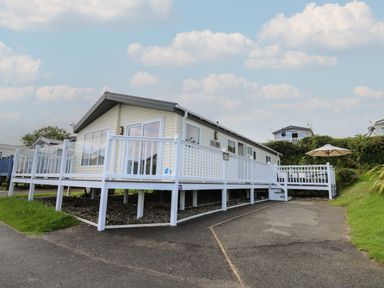 A mobile home with white railings and a patio umbrella at The Potting Shed in New Quay