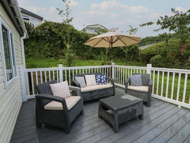 An outdoor patio with wicker chairs table umbrella and cushions surrounded by a white railing at The Potting Shed in New Quay