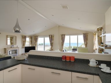 A kitchen with black countertops and white cabinets overlooking a living area with windows showing a sea view at The Potting Shed in New Quay