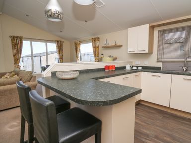 A kitchen with black chairs at a countertop and a living room with a sofa and yellow curtains at The Potting Shed in New Quay