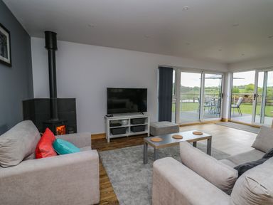 A living room with sofas a TV a wood burner and large glass doors leading to a patio and garden at Llyn Cae Ty Nant Fishery Holiday Let in Bwlchllan near Llangeitho