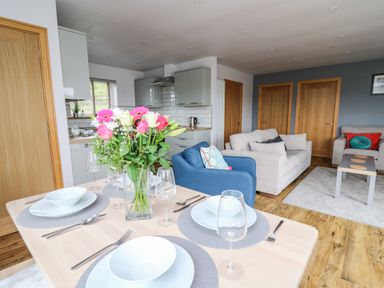 A dining table set with plates and glasses with flowers on it next to a living room with sofas and a coffee table at Llyn Cae Ty Nant Fishery Holiday Let in Bwlchllan near Llangeitho