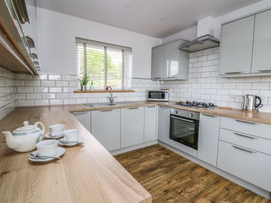 A kitchen with grey cabinets wooden countertops a gas stove oven microwave and tea set at Llyn Cae Ty Nant Fishery Holiday Let in Bwlchllan near Llangeitho