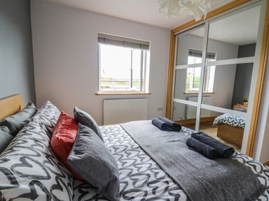A bedroom with a bed with heart-patterned bedding, pillows, towels, a window, and mirrored wardrobe at Llyn Cae Ty Nant Fishery Holiday Let Bwlchllan near Llangeitho