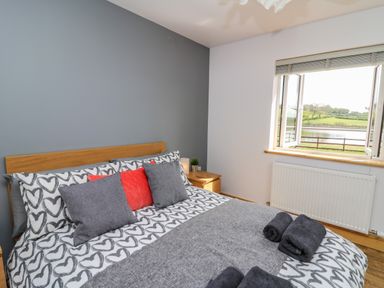 A bedroom with a bed with heart patterned bedding and a window showing a view of a lake at Llyn Cae Ty Nant Fishery Holiday Let in Bwlchllan near Llangeitho