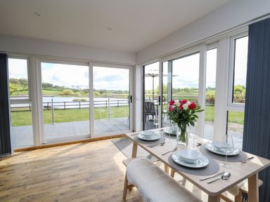 A dining area with a table set for four and a view of a lake through large glass sliding doors at Llyn Cae Ty Nant Fishery Holiday Let in Bwlchllan near Llangeitho