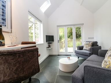 A living room with gray sofa and armchair and white round coffee table with glass door to a garden at Twigs in Woody Bay