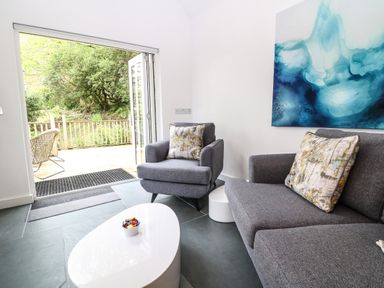 A living room with gray armchairs and a sofa with patterned cushions and a white coffee table with candy at Twigs in Woody Bay