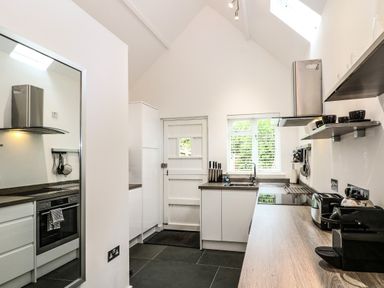 A kitchen with a countertop, sink, stove, oven, knives, coffee machine, toaster, shelves with cups, and a door at Twigs in Woody Bay