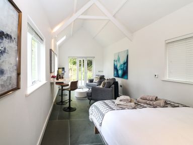 A bedroom with a bed, two chairs at a small table, a sofa, a round coffee table, and large windows at Twigs in Woody Bay