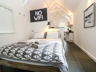 A bedroom with a bed and folded towels with a no wifi sign and kitchenette at Twigs in Woody Bay
