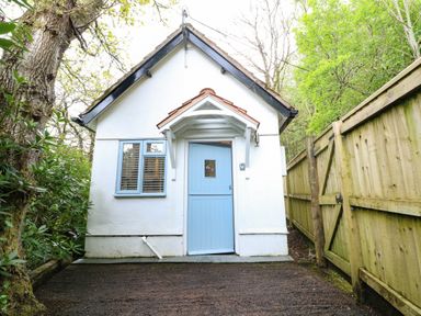 A small house with a blue door white walls a window a wooden fence and trees at Twigs in Woody Bay