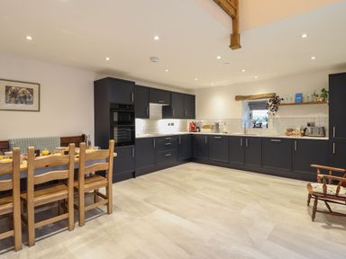 A kitchen with dark cabinets white countertops a dining table with wooden chairs and a wooden armchair at Merddwr in Cerrigydrudion