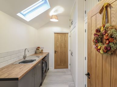 A utility room with a wooden countertop a sink washing machine wooden doors and cabinets at Merddwr in Cerrigydrudion