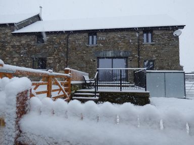 A stone house with a snow-covered roof and garden gate during snowfall at Merddwr in Cerrigydrudion