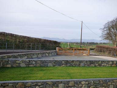 A stone-walled garden with a wooden gate and a grassy field with sheep in the background at Merddwr in Cerrigydrudion
