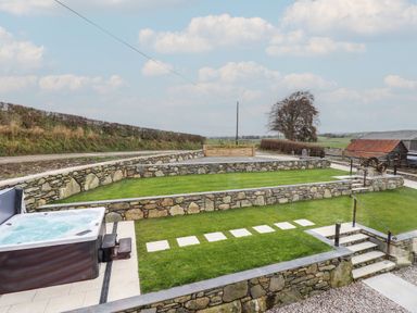 A tiered garden with stone walls and a hot tub at Merddwr in Cerrigydrudion