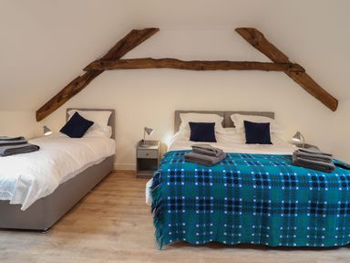 A bedroom with two beds wooden beams on the wall and bedside tables with lamps at Merddwr in Cerrigydrudion