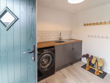 A utility room with a washing machine a sink wooden boot racks and coat hooks at Merddwr in Cerrigydrudion