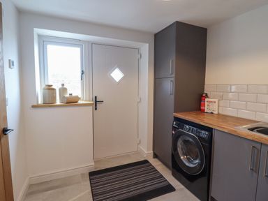 A utility room with a washing machine wooden countertop cabinets and a door with window at Merddwr in Cerrigydrudion