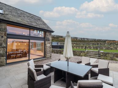 An outdoor patio with a table and cushioned chairs outside a stone building at Merddwr in Cerrigydrudion