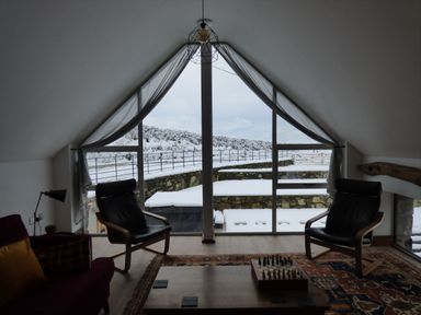 A room with two black chairs a coffee table with a chessboard and large triangular windows showing a snowy outdoor area at Merddwr in Cerrigydrudion