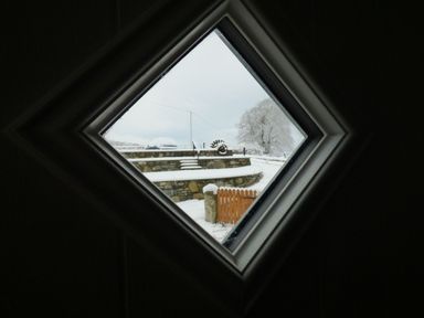 A snowy outdoor scene with stone steps and a wooden gate viewed through a diamond-shaped window at Merddwr in Cerrigydrudion