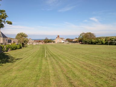 A grassy sports field with goalposts and houses in the background at Sea Pink Cottage in Langton Matravers