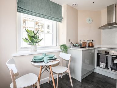 A small kitchen with a round table set for two green dishes white chairs a window with a green blind and kitchen appliances at Nantlle in Caernarfon