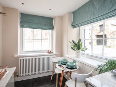 A small dining area with a round table set for two near two windows with blue roman blinds at Nantlle in Caernarfon
