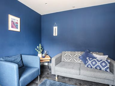 A living room with blue walls a blue armchair a grey sofa with cushions and a small wooden side table with plants at Nantlle in Caernarfon