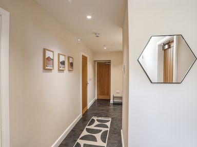 A hallway with three framed pictures on one wall a patterned rug on the floor two wooden doors and a hexagonal mirror on the opposite wall at Nantlle in Caernarfon
