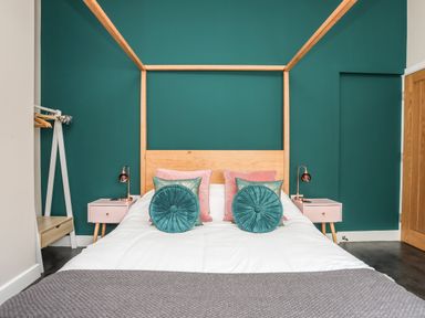 A bedroom with a wooden bed frame green wall pink bedside tables and pillows at Nantlle in Caernarfon