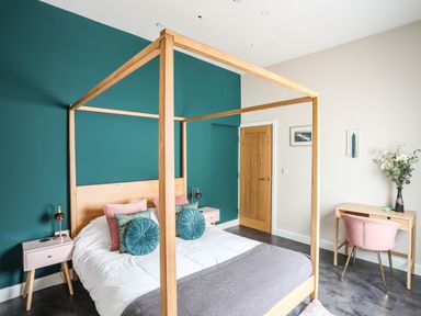 A bedroom with a wooden four-poster bed a green accent wall pink and green cushions bedside tables desk and chair with flowers at Nantlle in Caernarfon