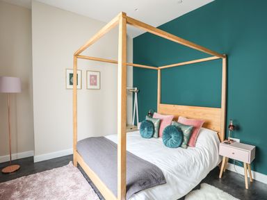A bedroom with a wooden four-poster bed teal and pink pillows and a nightstand at Nantlle in Caernarfon