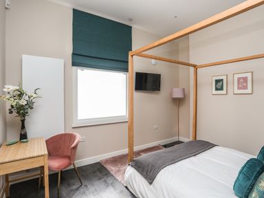 A bedroom with a four-poster bed a desk with flowers on it and a pink chair at Nantlle in Caernarfon