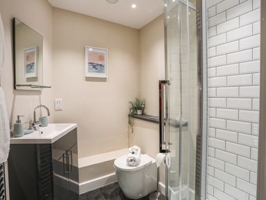 A bathroom with a shower area with white subway tiles a toilet with folded towels a black vanity with a sink and mirror and a framed picture on the wall at Nantlle in Caernarfon