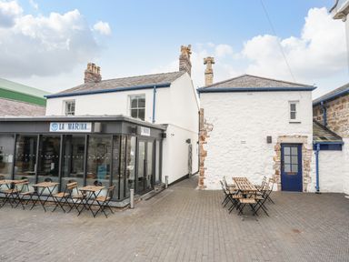 Outdoor seating area with wooden tables and chairs beside white buildings at La Marina in Caernarfon