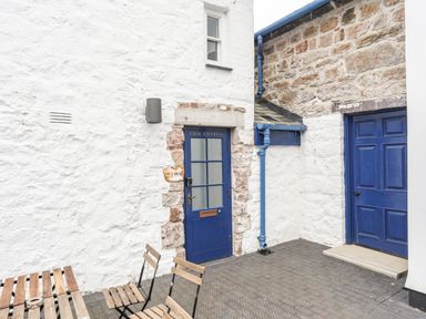 An outdoor area with white stone walls two blue doors wooden table and chairs at Nantlle in Caernarfon