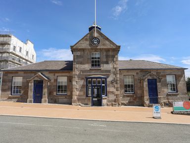 A stone building with blue doors and windows a clock and signs outside at Nantlle in Caernarfon