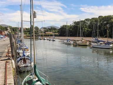 A marina with sailboats docked along a quay and more boats anchored in the water at Nantlle in Caernarfon