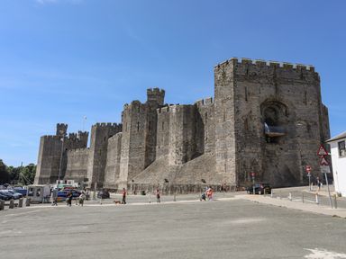 A medieval stone castle with battlements and towers with people walking nearby at Nantlle in Caernarfon