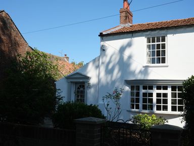 A white house with a tiled roof surrounded by bushes and a black metal gate at Phloxhaven in Reedham