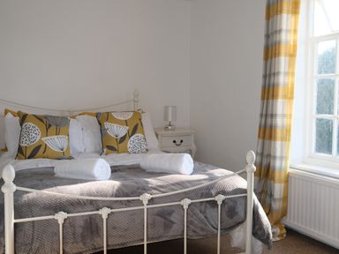 A bedroom with a white metal bed frame white bedside table and yellow plaid curtains at Phloxhaven in Reedham