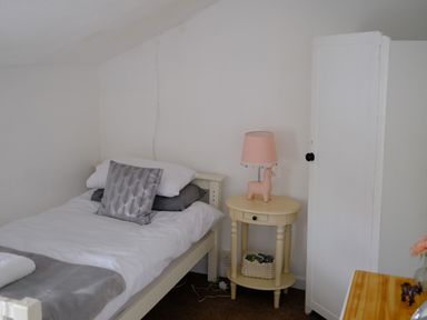 A bedroom with a single bed pillows and blanket a small round bedside table with a lamp and a basket and a white wardrobe at Phloxhaven in Reedham
