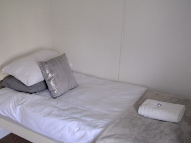 A single bed with white and gray pillows and a folded towel with a small heart on the blanket at Phloxhaven in Reedham