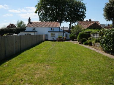 A white house with a red tiled roof and a wooden fence around a large grassy garden at Phloxhaven in Reedham