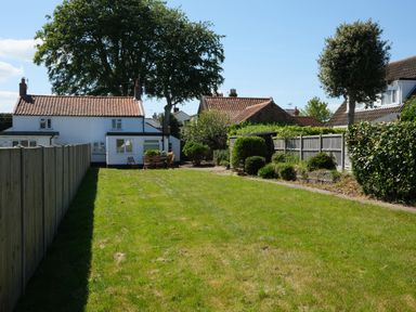 A backyard with grass and a table with chairs next to a white house at Phloxhaven in Reedham