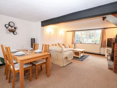An open plan living and dining area with a wooden dining table set and beige sofas near a window at Phloxhaven in Reedham