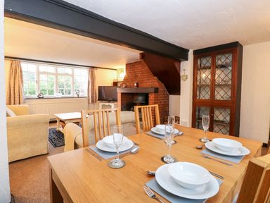 A dining area with a wooden table set for four and a living area with sofas a television and a brick fireplace at Phloxhaven in Reedham